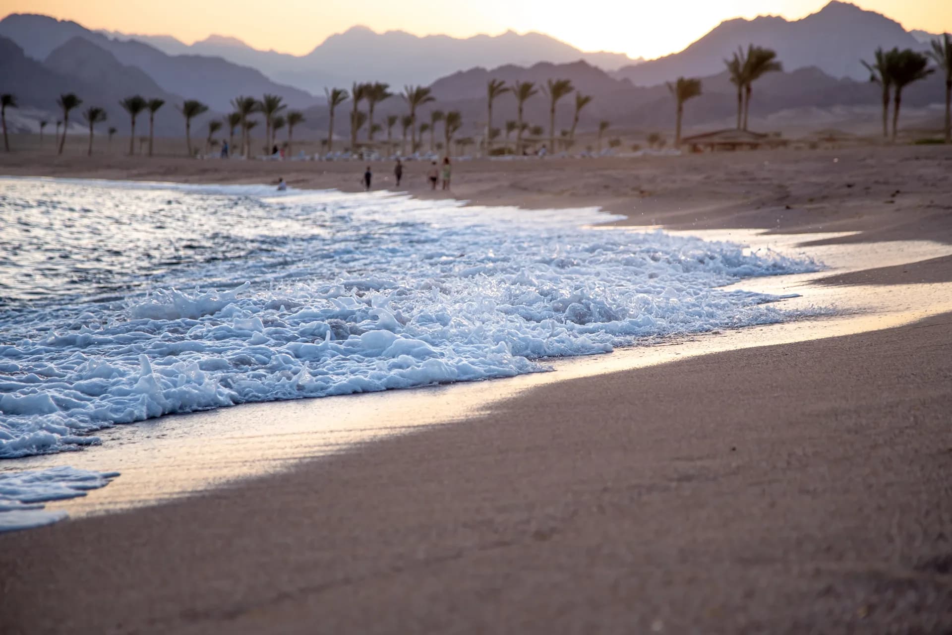 Sandy beach at golden hour with the Hajar Mountains on the horizon